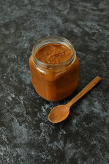 Jar with zucchini caviar and wooden spoon on black smokey background