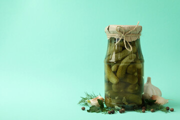 Jar of pickled cucumbers and ingredients on mint background