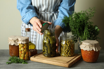 Woman closes a jar of pickled cucumbers on wooden background with pickled food
