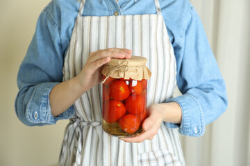 Woman in apron hold jar of pickled tomatoes
