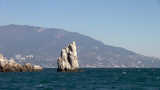 Black Sea waves of emerald color are broken on Sail rock. Southern coast of Crimea. Rock Sail grew out of depths of ea against backdrop of Crimean mountains stretching into water.