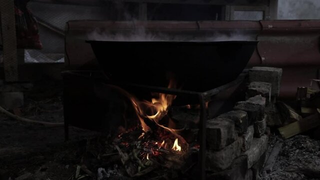 The meat is cooked in a cauldron. Night time. A slow fire burns and steam comes out of the cauldron.