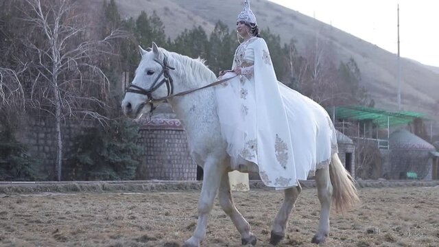 An Asian girl in a national costume is riding a horse. Kyrgyz national costume.