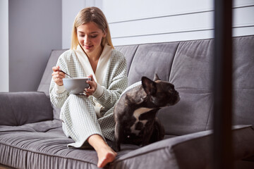 Female with a dog eating from bowl on sofa