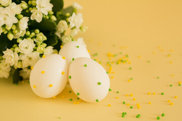 The religious holiday of Easter. White Easter eggs with polka dots on a yellow background with flowers. copy space. Religious traditions. Easter egg design.