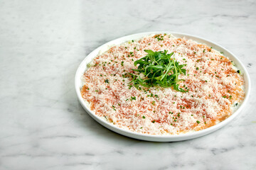 Classic Italian appetizer - salmon carpaccio with arugula and parmesan, served on a white plate on a marble background. Thinly sliced salmon. Restaurant seafood.