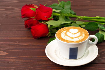 Obraz premium Cup of cappucino with art and bouquet of roses on wooden table