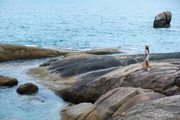 A woman standing on the rock by the seashore with blue sky background