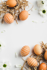 Frame of Easter eggs in nests and spring flowers on white background. Happy Easter vertical banner mockup. Flat lay, top view, copy space.