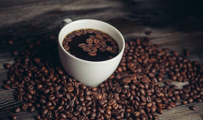 coffee beans scattered on a wooden table and a cup with a hot drink aroma
