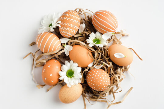 Nest with easter eggs and spring flowers on white background. Happy Easter concept. Flat lay, top view.