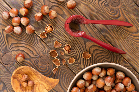 Hazelnuts with a red nutcracker in a bowl on a wooden board, nutshell, dark photo, flat lay