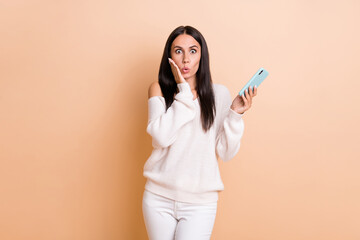 Fototapeta premium Photo of young woman amazed shocked surprised news fake novelty use smartphone isolated over beige color background
