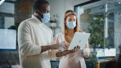 CTO and Chief Strategist Wearing Face Masks Talking About Business Growth, Analyze Data, Use Laptop Computer. Two Diverse Professionals Discuss Revenue Increase, Market Disruption, Planning Strategy