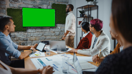Office Conference Room Meeting: Black Chief Company Strategist Doing Green Screen TV Presentation to a Diverse Team of Multi-Ethnic Businesspeople. Using Chroma Key Wall TV Monitor