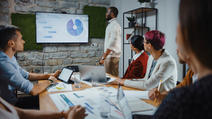 Office Conference Room Meeting: Black Chief Company Strategist Doing TV Presentation to a Diverse Team of Multi-Ethnic Professional Businesspeople, Explaining Marketing Strategy, Data Analysis