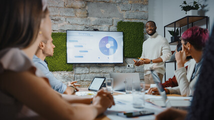 Office Conference Room Meeting: Black Chief Company Strategist Doing TV Presentation to a Diverse Team of Multi-Ethnic Professional Businesspeople, Explaining Marketing Strategy, Data Analysis