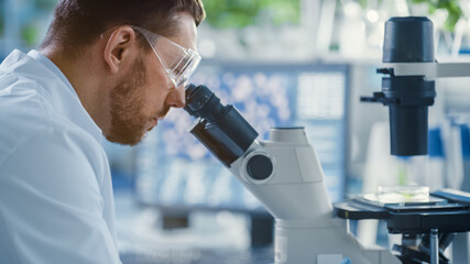 Shot of a Handsome Male Scientist Looking into the Microscope. Medical Scientist Working in a Modern Food Science Laboratory with Advanced Technology Microscopes and Computers.