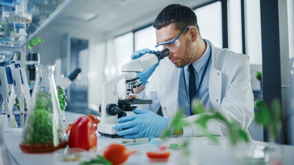 Male Microbiologist Looking at a Lab-Grown Cultured Vegan Meat Sample in a Microscope. Medical...