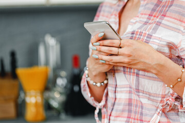 Unrecognizable woman using smartphone in kitchen close up