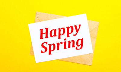 On a yellow background, an envelope and a card with the text HAPPY SPRING. View from above
