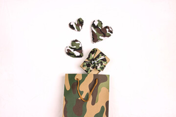 Khaki shopping bag with gift box and camouflage hearts on white background. Defender of the Fatherland Day, February 23.
