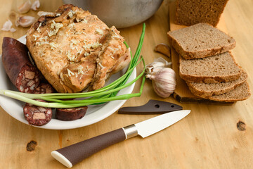 baked meat and blood sausage on a plate, green onion and garlic on wooden background, home cooking