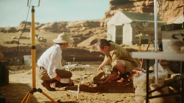 Archeological Digging Site: Two Great Archeologists Work on Excavation Site, Carefully Cleaning, Lifting Newly Discovered Ancient Civilization Cultural Artifact, Historic Clay Tablet, Fossil Remains