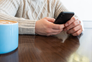 Young, handsome man drinking coffee and using smartphone in cafe. Online watching enjoyind reading social media. Shopping on the internet.