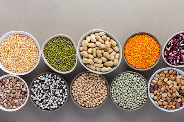Different types of legumes in bowls, green and yellow peas, chickpeas and peanuts, colored beans and lentils, mung beans and beans, top view