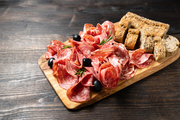 Sliced salumi salami on a wooden board with olives and multigrain baguette. italian food, appetizer for aperitif or salami sandwich. Top view