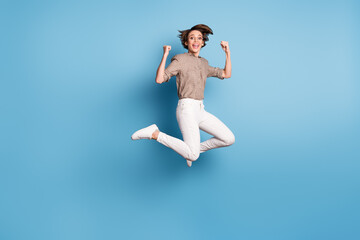 Fototapeta na wymiar Full length portrait of carefree lady jumping fists up open mouth celebrate isolated on blue color background