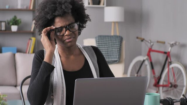 overwhelmed stressed black woman works at laptop computer at her desk,tired overworked female working from home taking off glasses massaging her neck has headache