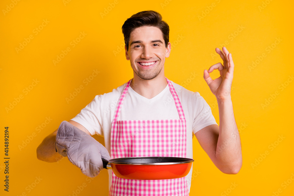 Sticker Photo portrait of guy in kitchen gloves showing ok-sign holding frying pan isolated on vivid yellow colored background