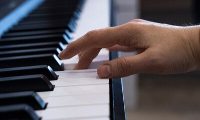 Obraz premium A female hand is playing the electronic digital piano at home. The woman is a professional pianist who arranges music using electronic piano keys. The musician practices keyboards and composes a