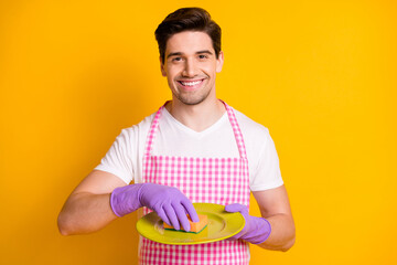 Photo portrait of man in rubber gloves washing dishes with sponge isolated on vivid yellow colored background