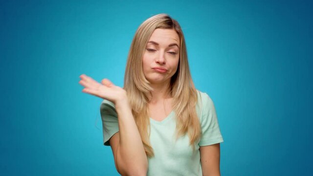 Young bored woman making blah-blah gesture with hand against blue background