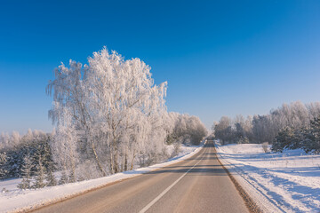 Obraz premium Winter landscape with the road the forest and the blue sky