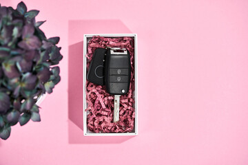 Surprise for her. Top view of a car key in present box and flowers on pastel pink background