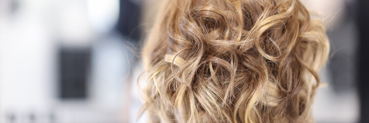 Woman with curly hair sit in beauty salon back view. Professional hairstyle close up concept.