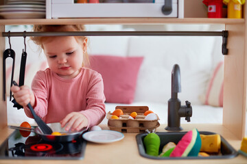 cute toddler baby girl playing on toy kitchen at home, pretends frying eggs - 414895916