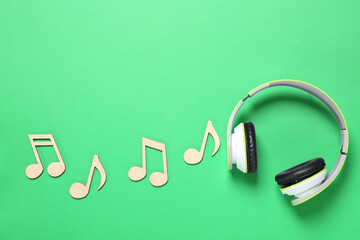 Wooden music notes and headphones on green background, flat lay