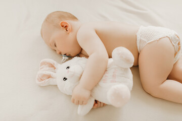 Little baby sleeping with plush toy-white hare in the crib
