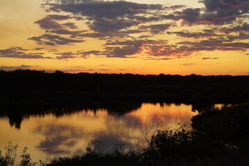 Bright yellow sunset over the forest and river with reflection and circles on the water. Clouds illuminated by purple light
