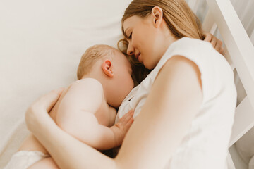 Beautiful young mom and her cute little baby sleeping in bed