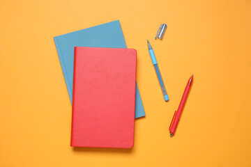 Stylish notepads and pens on orange background, flat lay
