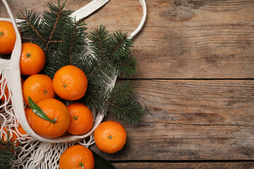 Fototapeta na wymiar Fresh ripe tangerines, fir tree branches and mesh bag on wooden table, flat lay. Space for text