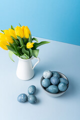 Still life with spring fresh flowers in white jug and Easter eggs in gray bowl.