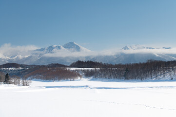 Fototapeta na wymiar 冬美瑛雲かかる雪山のある風景