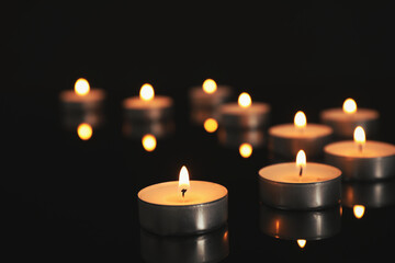 Many burning candles on black table in darkness